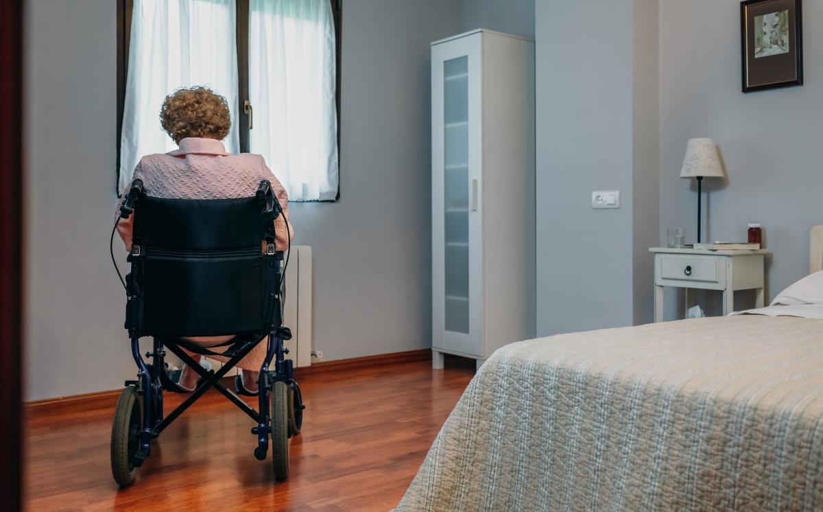 Elderly woman sitting in a wheelchair facing the window in a bedroom