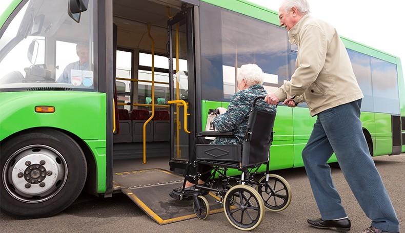 Older man pushing older woman onto city bus using ramp platform