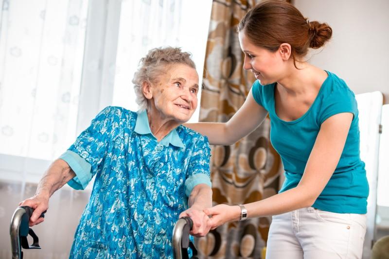 Young caregiver assisting older woman with rollator in home setting